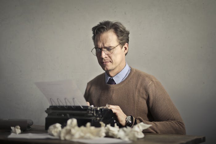 A thoughtful writer using a typewriter surrounded by crumpled paper, embodying vintage creativity.