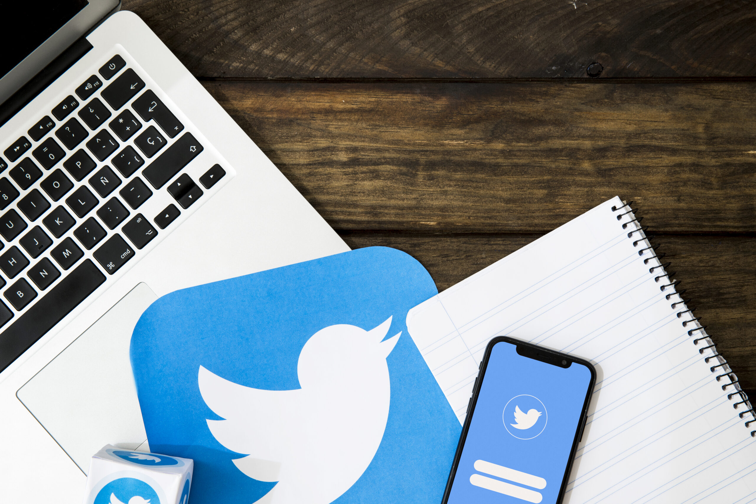 A laptop, a notepad, and a smartphone displaying the Twitter login screen are arranged on a wooden desk—an inspiring setup for consultants or coaches planning their next Twitter thread ideas. Uploaded on aifreeforever.com