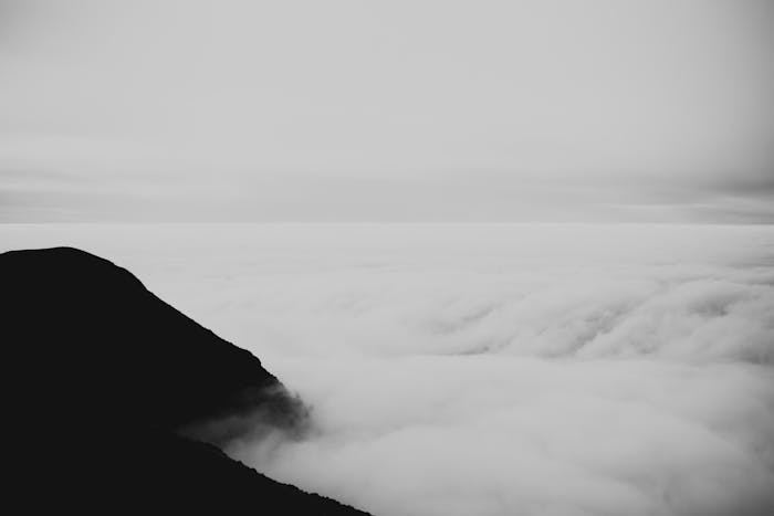 Dramatic black and white landscape of a mountain peak silhouetted against clouds.
