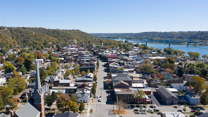 Aerial view of a picturesque small town by the river, surrounded by lush hills under a clear blue sky.