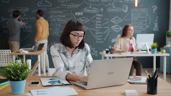 Woman working on laptop in modern office with team.